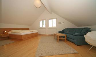 A cozy room with a bed, a couch, and a table. Large windows let in plenty of light.