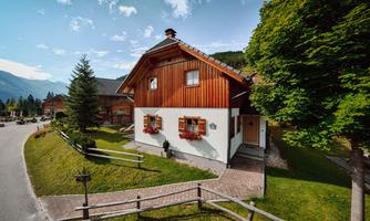 A charming house with wooden elements and flower windows. Surrounded by trees and a beautiful landscape.