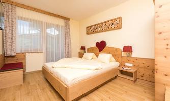 A cozy bedroom with a large bed and wooden details. The room decoration is simple and inviting, featuring a beautiful window and red accents.
