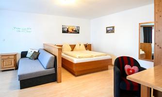 A comfortable room with a double bed, sofa, and table. Bright colors and a cozy atmosphere create an inviting space.