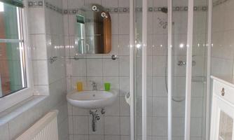 A modern bathroom with a shower and a small sink. The walls are tiled and there is a window for additional light.