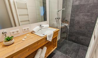 A modern bathroom with a shower cabin and a wooden shelf. On the shelf, there are towels and a small plant.