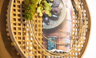 A decorative wall basket with plants and branches. Inside, there is a picture with a bowl and various objects.