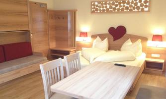 A cozy room with wooden interior, featuring a large bed and a dining table. The atmosphere is inviting and friendly.