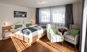 A modern bedroom with a large double bed and a comfortable armchair. 

Plenty of daylight streams through the windows, creating an inviting atmosphere.