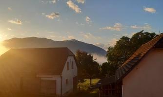 A picturesque landscape with a sunset behind the mountains. In the foreground, there are some houses and trees visible.