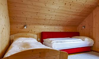 A cozy bedroom with wood paneling. There is a single bed and a double bed in a bright, inviting room.