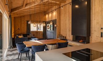 A stylish, modern living room with wood paneling and large windows. The dining area features a wooden table and upholstered chairs, providing a cozy atmosphere.