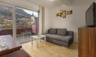 A modern living room with a gray sofa and a table. Large windows offer a view of the mountains and the city.