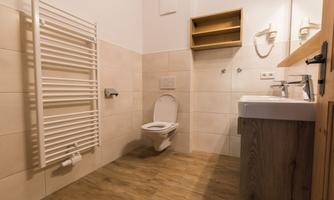A modern bathroom with a white toilet and a sink. The walls are light and there is a metal towel warmer.