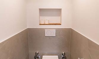 A modern bathroom with a toilet and a small sink. The walls are bright and the tiles are gray.