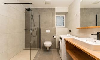 A modern bathroom with a walk-in shower and a sink on a wooden shelf. A washing machine and bright tiled walls are also visible.