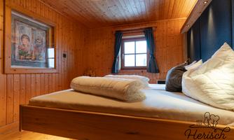 A cozy bedroom with wooden paneling and a large window. There is a double bed with fresh towels and a beautiful mural.