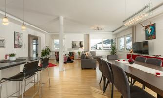A spacious living area with a modern dining area and comfortable seating. Large windows offer a beautiful view of the mountains.