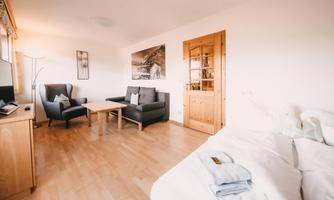 A bright room with a bed and a seating area. There are two cozy armchairs, a table, and a television.