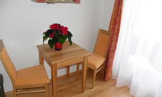 A small wooden dining table with two chairs. On the table, there is a flowering plant in a red pot.
