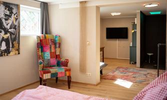 A cozy room with a colorful, striped armchair and a large window. The wooden floors and the television create an inviting atmosphere.