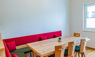A stylish dining area with a large wooden table and modern chairs. The cozy bench with red cushions provides additional seating.