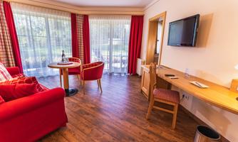 A bright room with wooden floors and large windows. Red furniture and a table create a cozy atmosphere.