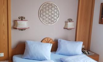 A cozy bedroom with two separate beds and bright pillows. Decorative lamps and a piece of artwork hang on the wall.