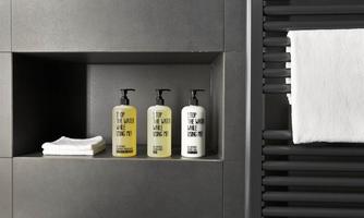 Three bottles of care products are standing on a shelf in a modern bathroom. Next to the bottles are folded towels.