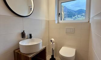 A modern bathroom with a round mirror and a stylish sink on a wooden base. The window offers a view of the mountains.