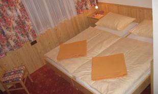 A cozy bedroom with a double bed and orange bedding. The walls are made of wood and the windows are decorated with floral curtains.