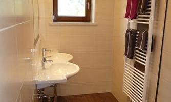 A modern bathroom with two sinks and a towel radiator. The window provides natural light and a bright atmosphere.