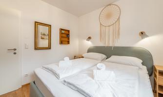 A modern bedroom with two beds and fresh towels. Decorations are hanging on the wall, and the room is bright and inviting.
