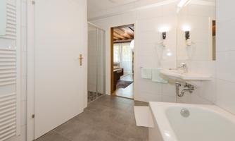 A modern bathroom with white tiles and a bathtub. The room is bright and inviting, with a separate shower and a window.