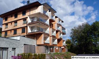 A modern building with wooden cladding and several balconies. It is located in a natural environment with green trees.