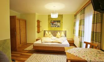 A cozy bedroom with a large bed and light wooden floor. There is a small seating area with a table and a chair.