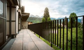 A modern balcony with tiled view of green meadows and mountains. The sky is cloudy and there is a calm atmosphere.