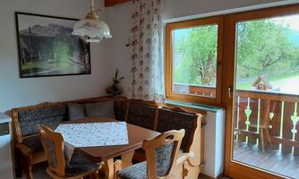 A cozy dining area with a wooden table and a bench. The view of the greenery is visible through the windows.