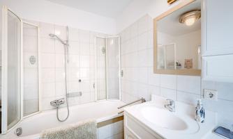 A modern bathroom with a bathtub and a separate shower. Bright tiles and large mirrors create a friendly atmosphere.