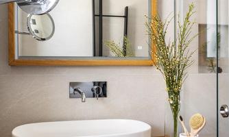A modern bathroom with a white sink on a wooden shelf. The large mirror reflects the stylish decor and the glass shower.