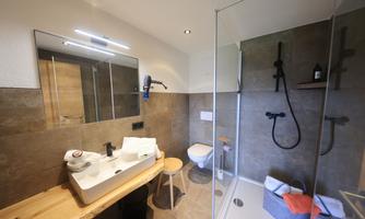 A modern bathroom with a shower, a sink, and a toilet. It is bright and friendly with stylish tiles and wooden details.