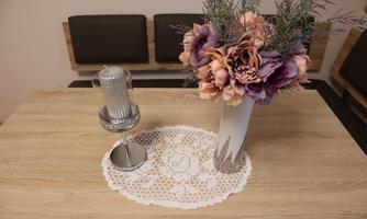 A table with an elegant tablecloth, on which a candle and a vase with colorful artificial flowers are placed. The atmosphere is cozy and inviting.