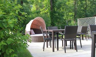 A beautiful garden area with a large rattan sofa and a table with chairs. Surrounded by green trees and plants, it is an ideal place to relax.