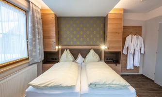 A modern bedroom with two beds and an elegant wood design. In the background, bathrobes hang on the door.