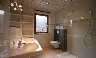 A modern bathroom with white tiles and a large window. There are two sinks, a shower, and a toilet.