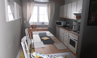 A bright kitchen with a large dining table and white chairs. The walls are painted in neutral colors, and there are windows that let in daylight.