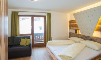 A modern bedroom with a double bed and a cozy couch. The room has large windows with a view of the snowy landscape.