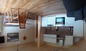 A modern kitchen with a dining area and a living room. The room has hardwood floors and large windows.