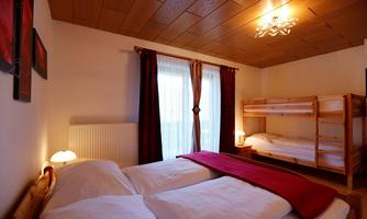A cozy bedroom with a double bed and a bunk bed. The room has large windows and warm colors.