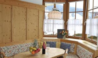 An inviting dining area with a round table set and an upholstered bench. Large windows provide plenty of daylight and a cozy atmosphere.