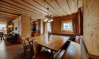 A cozy dining area with a large wooden table and chairs. The walls and ceiling are made of wood, and the lighting creates an inviting atmosphere.