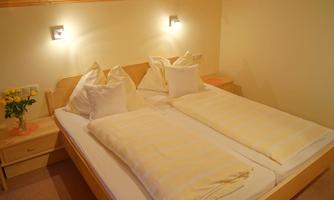 A cozy bedroom with a double bed and soft pillows. Next to the bed is a table with a flower vase.