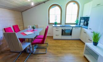 A modern kitchen with a dining area. The room has large windows and is designed to be bright and inviting.