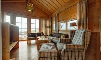A cozy living space with wooden paneling and large windows. The decor is bright and inviting, with comfortable seating and views of nature.